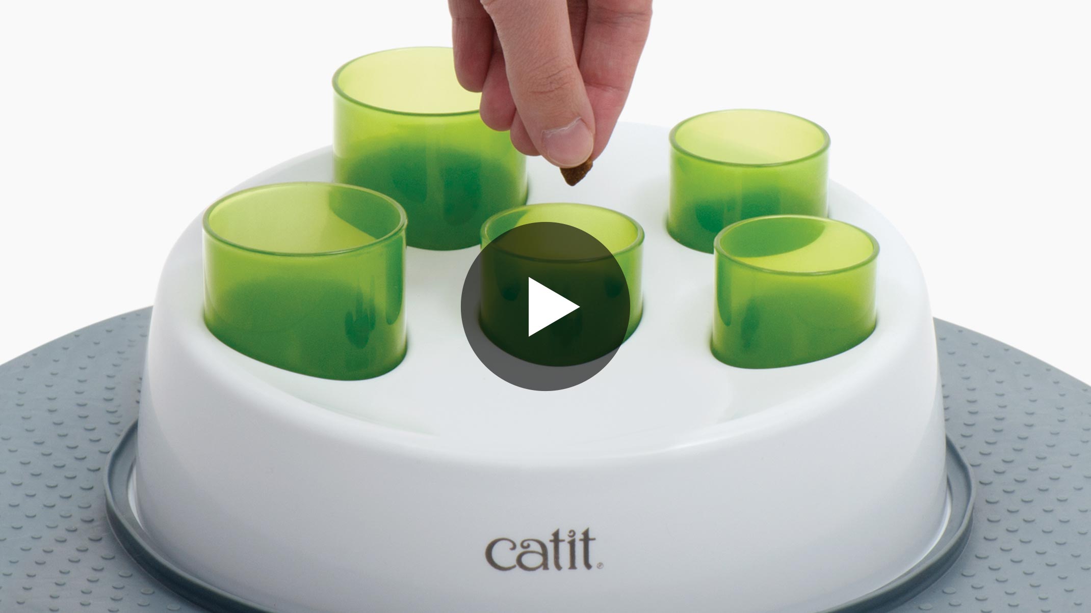A hand placing a treat into a green tube on a Catit Senses Digger cat toy