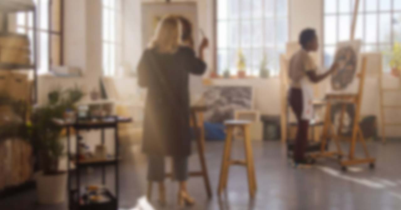 Two people painting on canvases in a bright, sunlit art studio