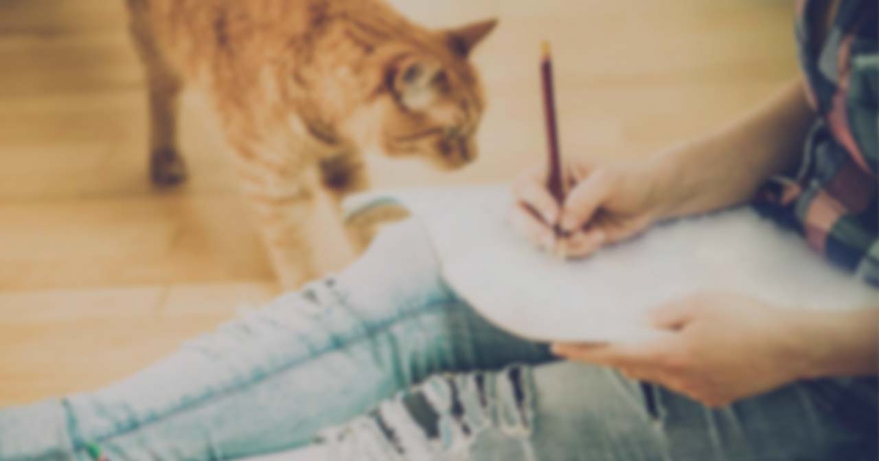A person sitting on the floor writing on a piece of paper while an orange cat watches them
