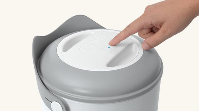 A finger pressing the power button on the lid of a Catit PIXI Smart Vacuum Food Container