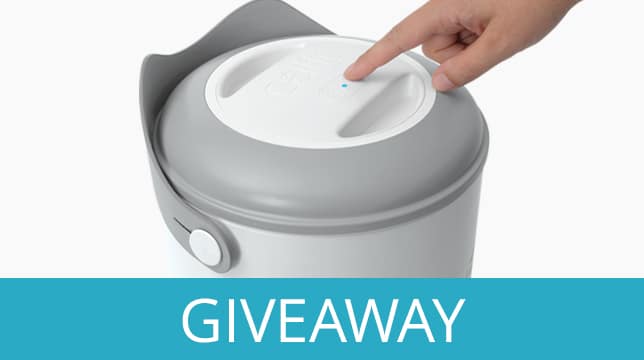 A hand pressing the button on a Catit PIXI Smart Feeder for a giveaway