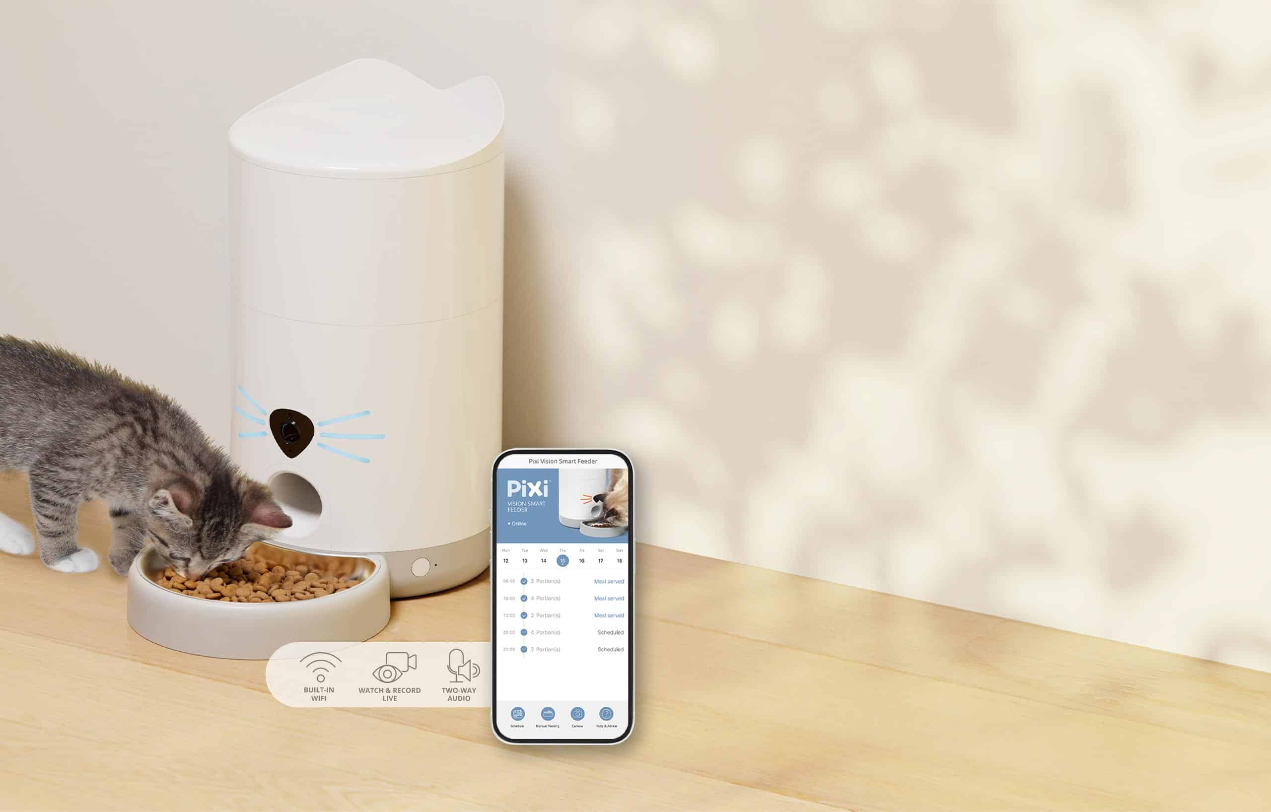 A kitten eats from a PIXI Vision Smart Feeder, shown alongside a smartphone displaying the companion app interface
