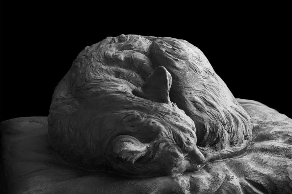 A clay sculpture of a cat curled up and sleeping on a cushion