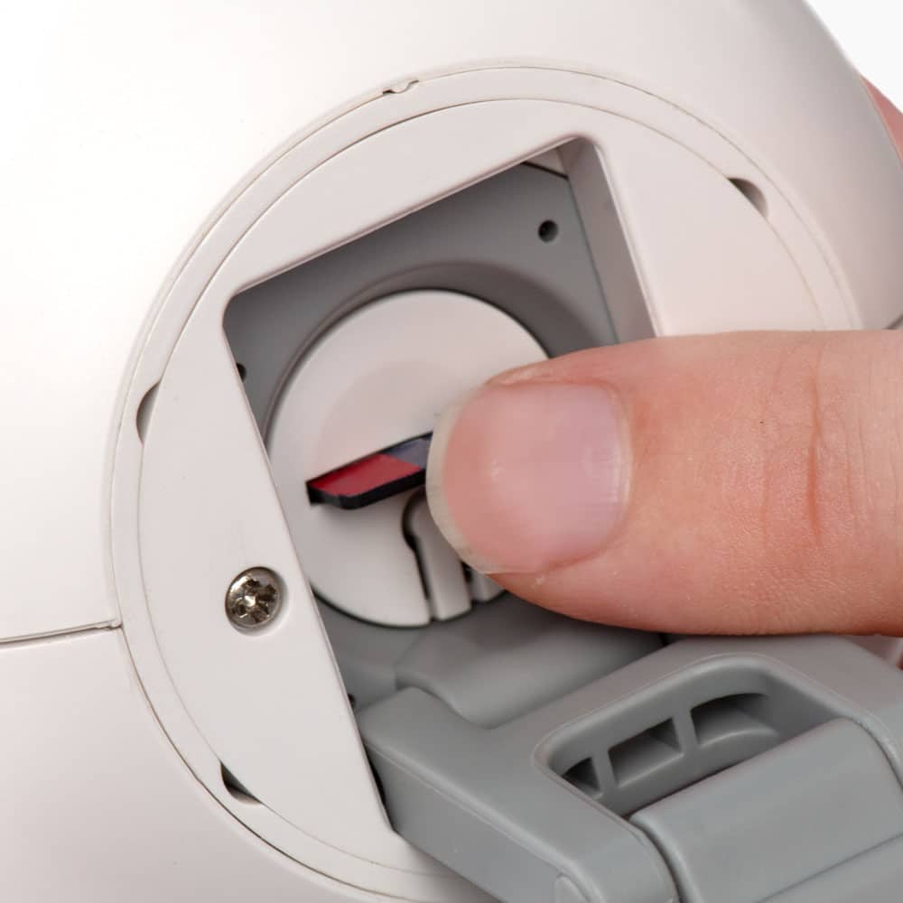 A finger pressing a small red button on the back of a white Catit PIXI camera device