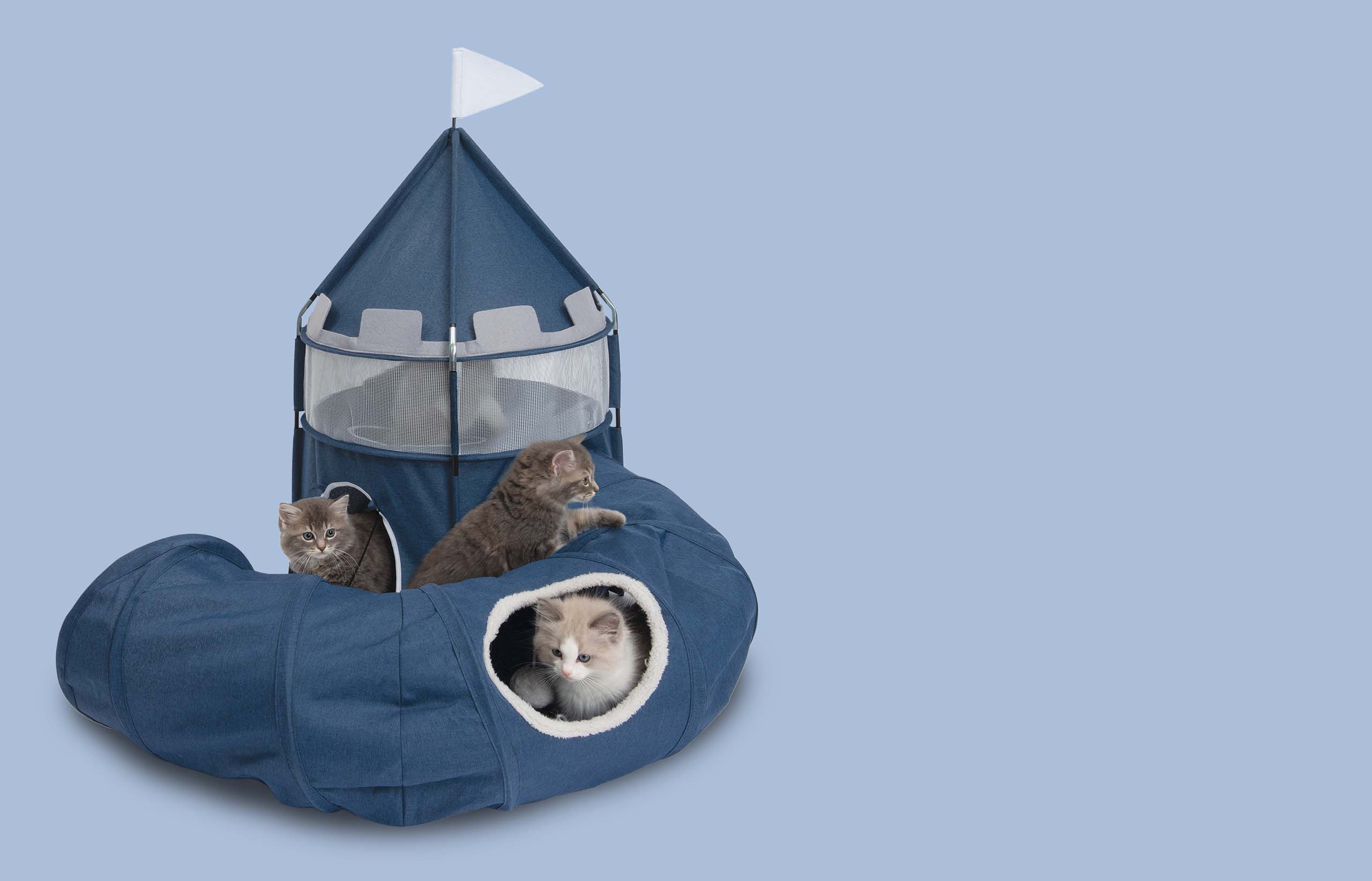 Three kittens playing in and around a blue fabric castle-shaped cat tunnel and hideaway on a light blue background