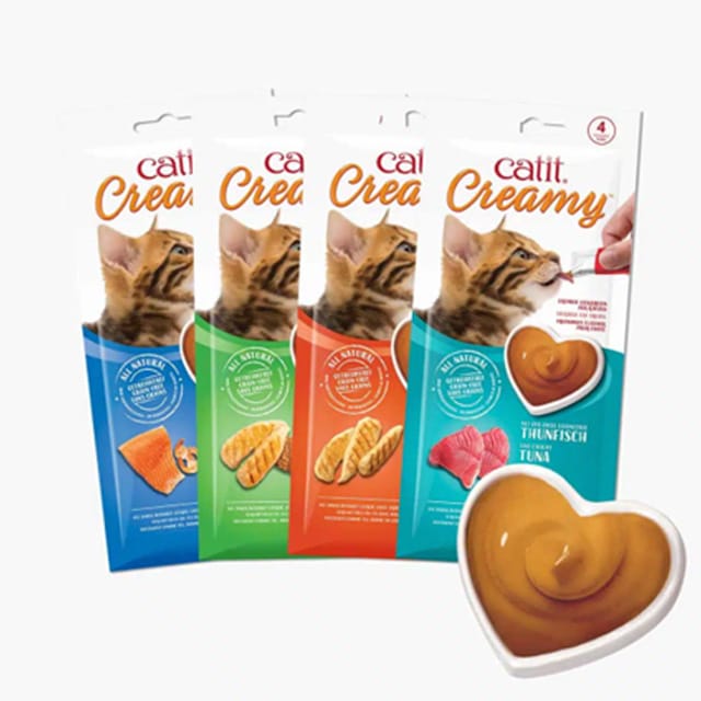 Four packages of Catit Creamy cat treats in various flavors, with a heart-shaped dish of the creamy treat in the foreground