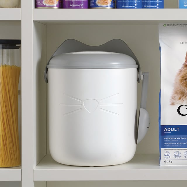 White PIXI vacuum food container with grey cat-ear lid and scoop, sitting on a shelf next to cat food packaging