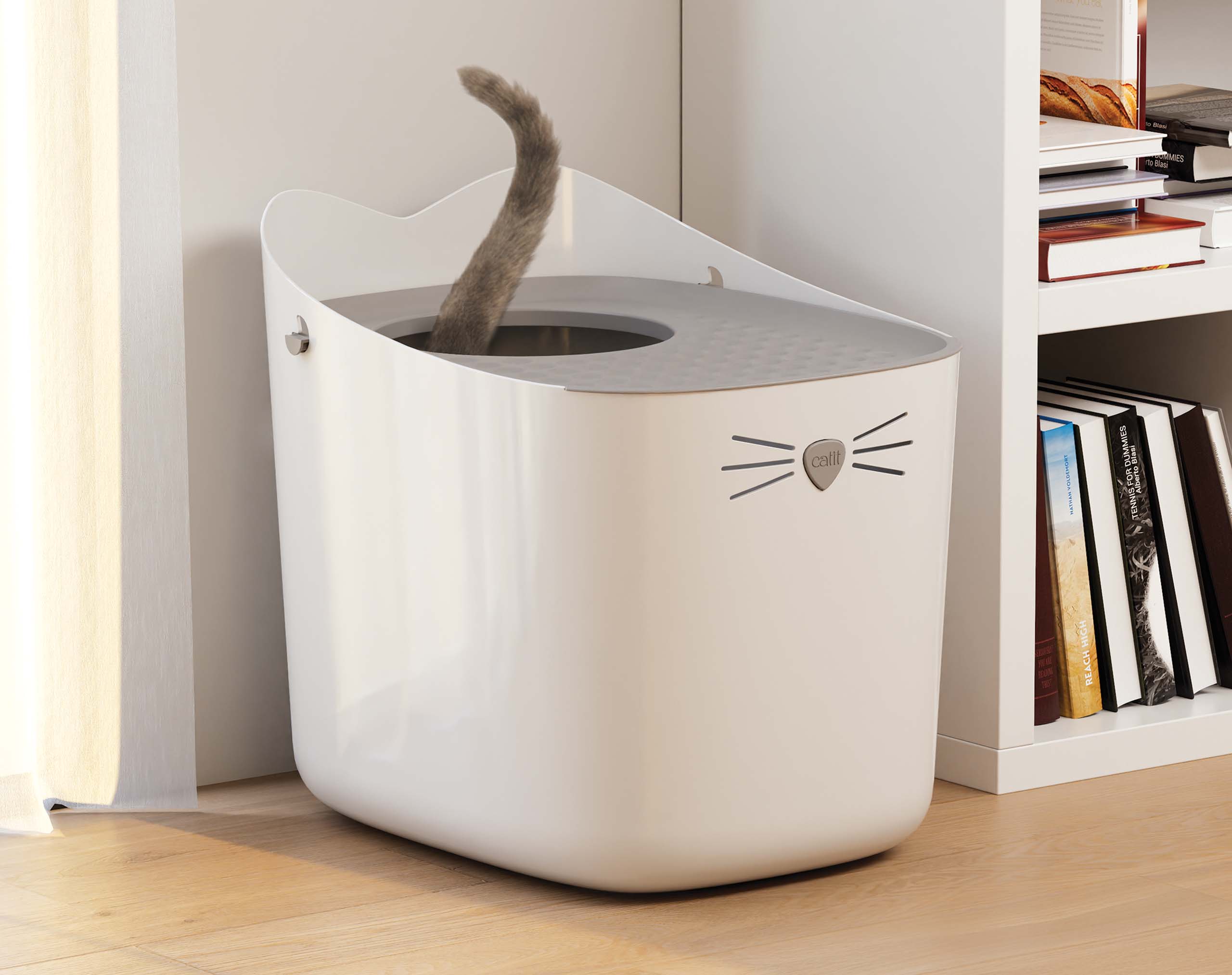 Catit cat litter box with a grey lid and a cat tail visible inside, placed next to a bookshelf