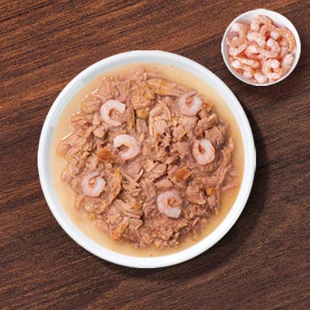A white bowl filled with shredded tuna and shrimp cat food, with a small side dish of shrimp on a wooden surface
