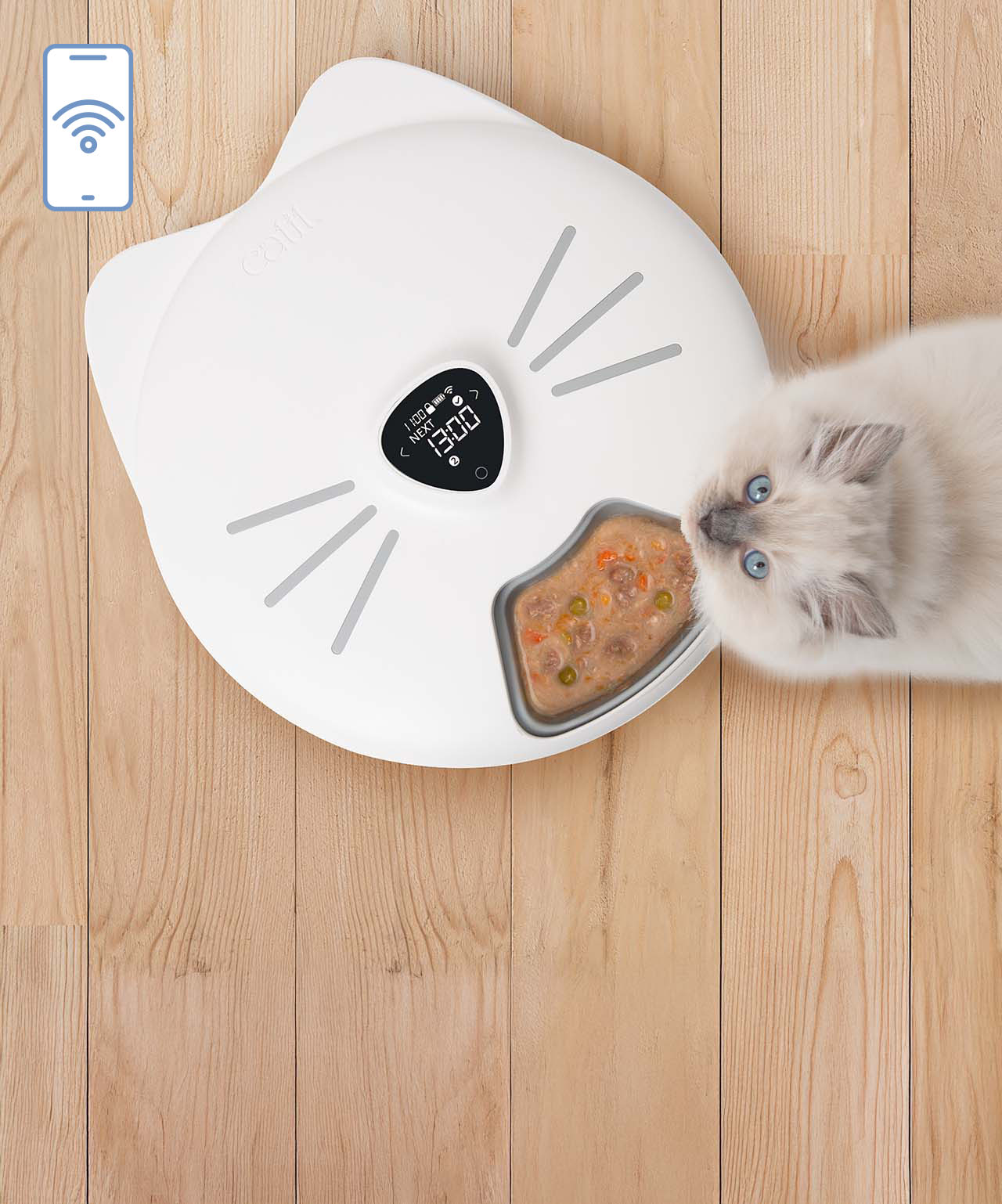 Wifi supported white cat-shaped PIXI smart feeder with a digital display and a bowl of wet food, next to a fluffy cat on a wooden floor
