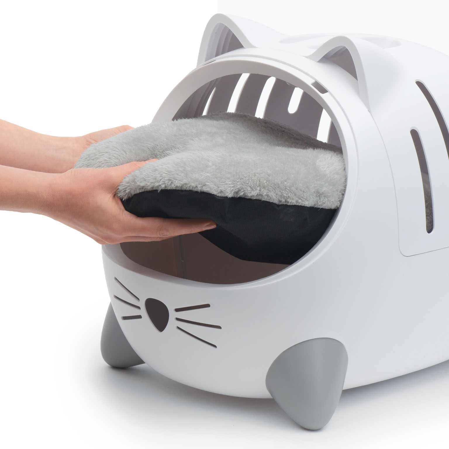 Hands placing a soft, grey, plush cushion into a white, cat-shaped pet carrier