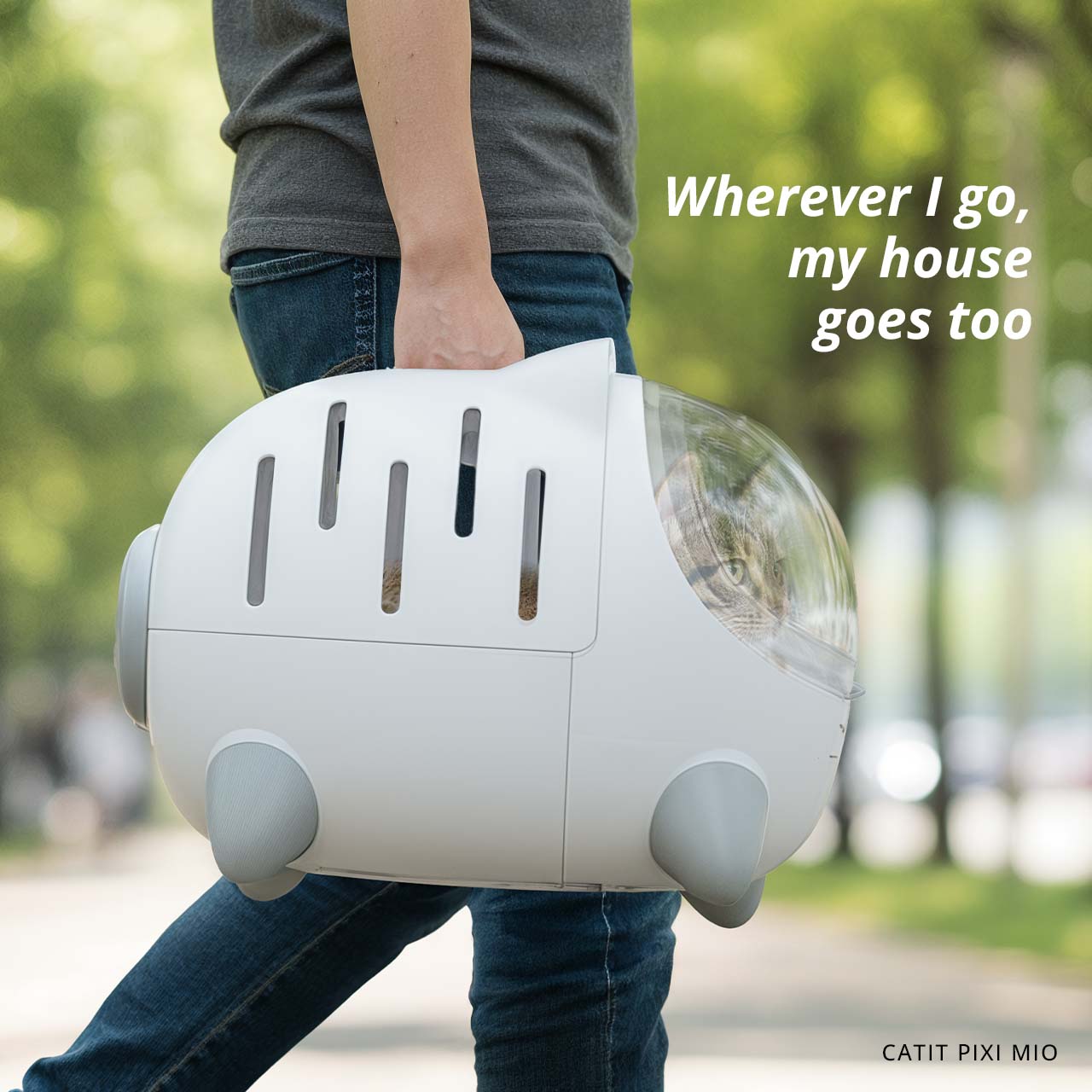 A person carries a white Catit PIXI MIO cat carrier with a cat visible inside through a clear bubble window