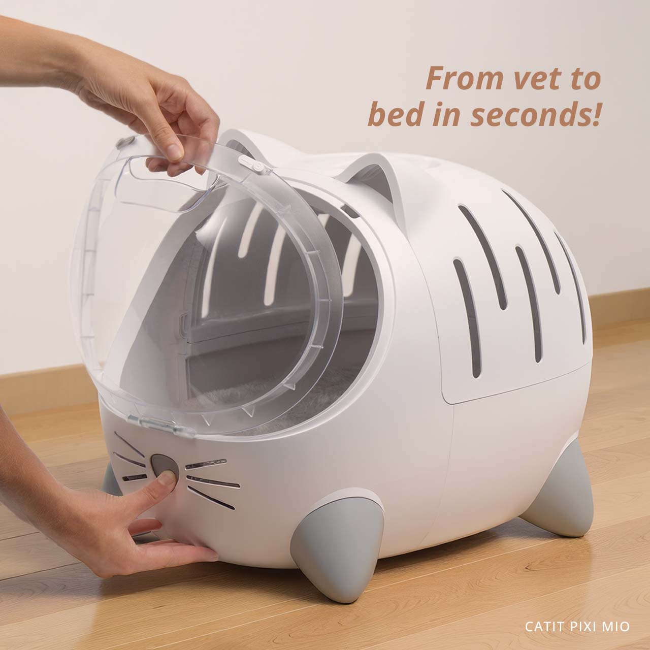 A person opening the clear front door of a white, cat-shaped PIXI MIO pet carrier on a wooden floor