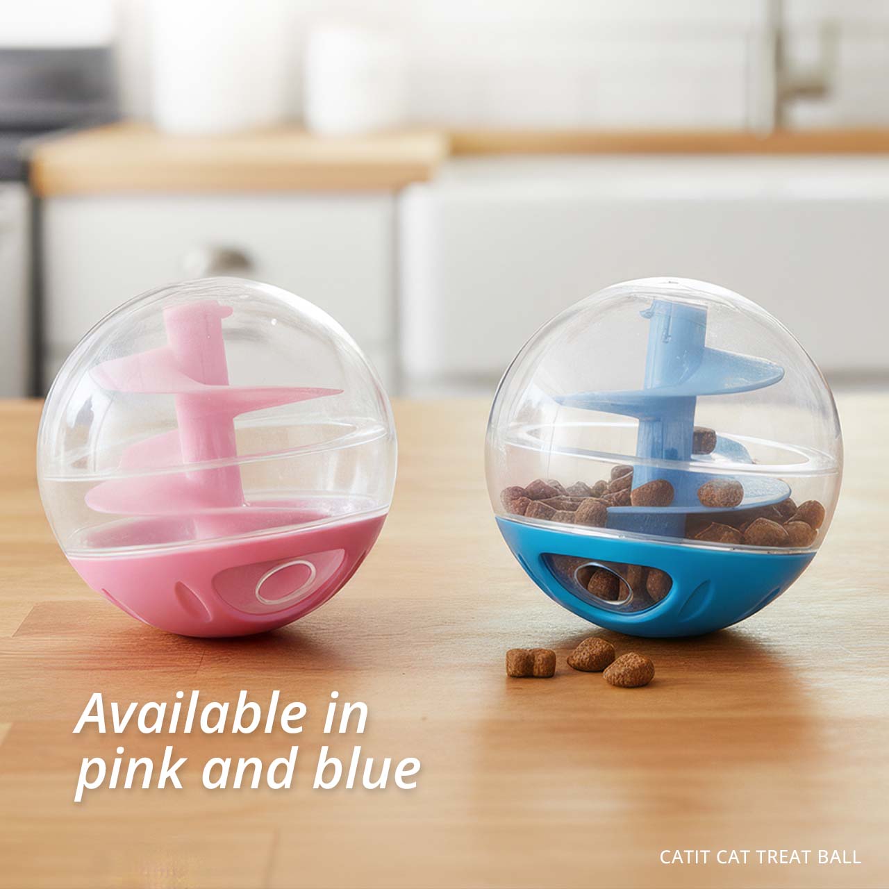 Catit treat balls in pink and blue sitting on a wooden surface with treats spilling out