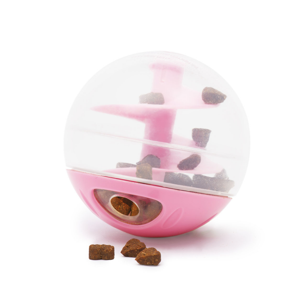 Pink and clear plastic treat-dispensing ball toy for cats with dry food inside and on the surface below