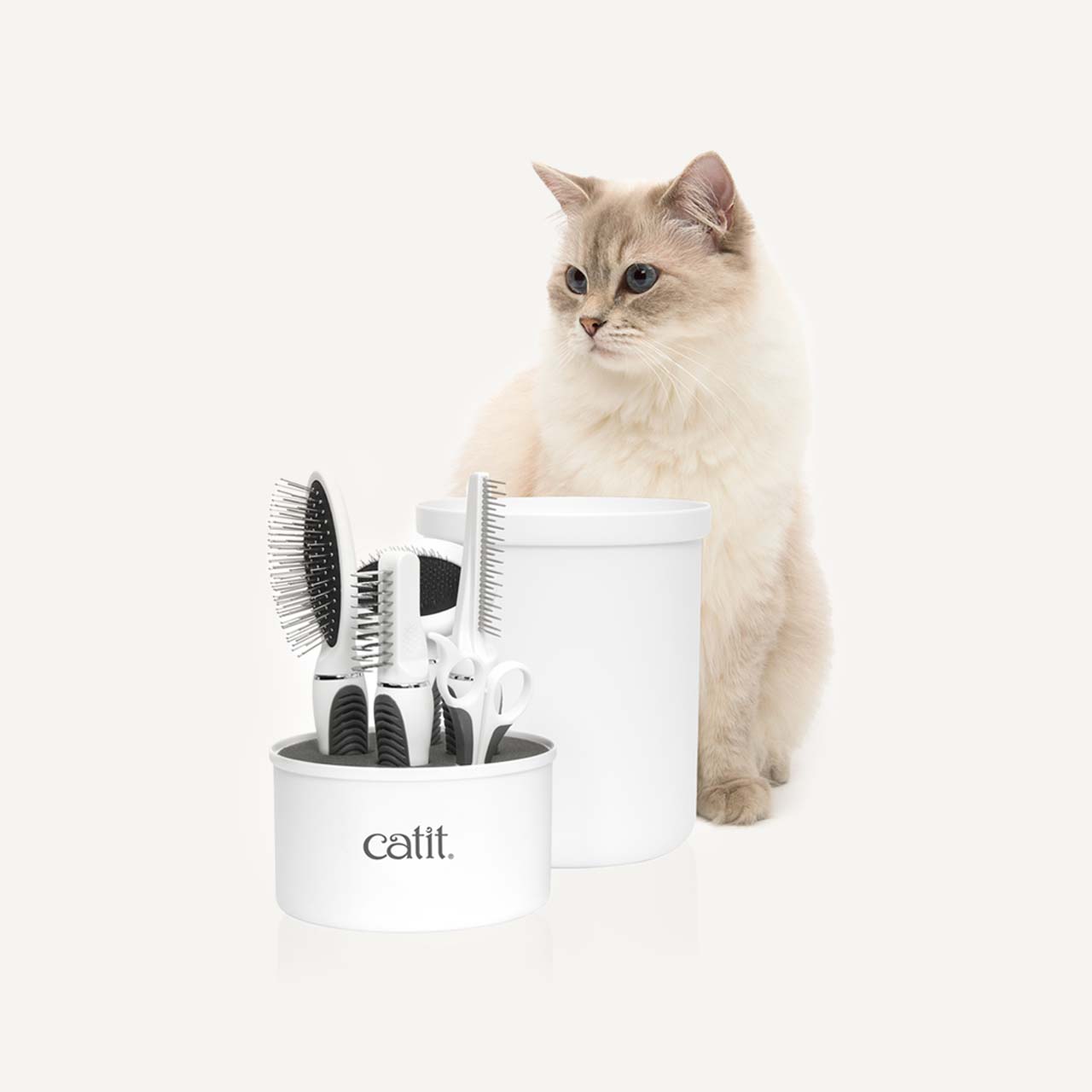 Catit longhair grooming kit with various brushes and combs in a white storage container next to a fluffy cat