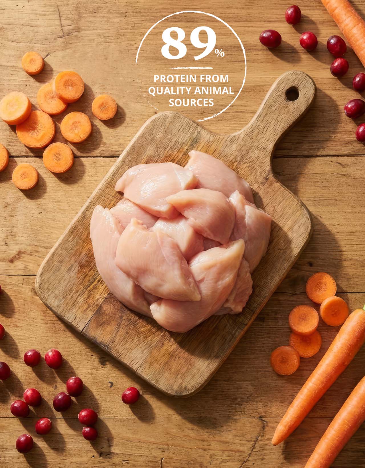 Raw chicken pieces on a wooden cutting board surrounded by carrots and cranberries with text stating 89% protein from quality animal sources