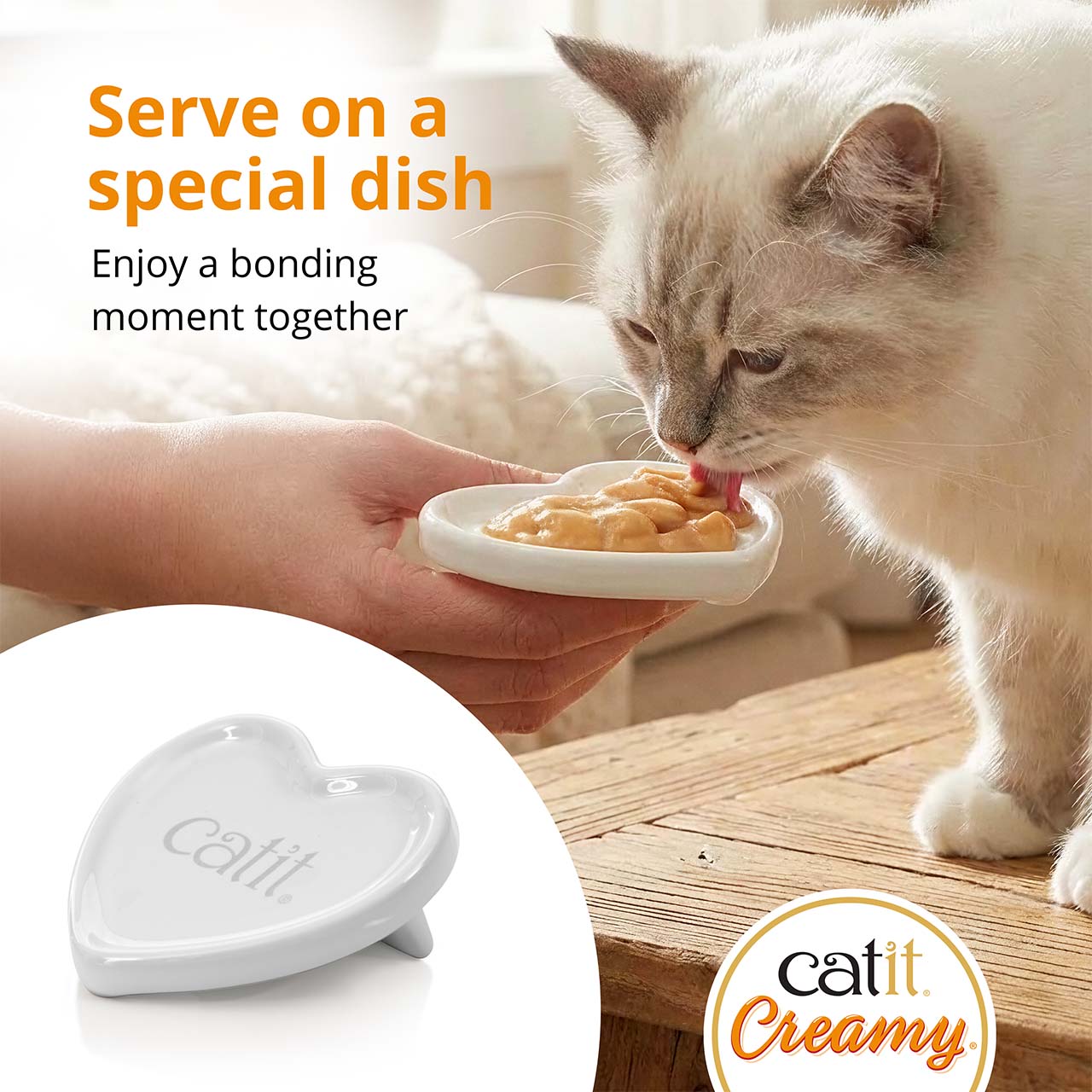 A person holds a heart-shaped Catit dish while a cat licks creamy treat from it, promoting bonding time with Catit Creamy