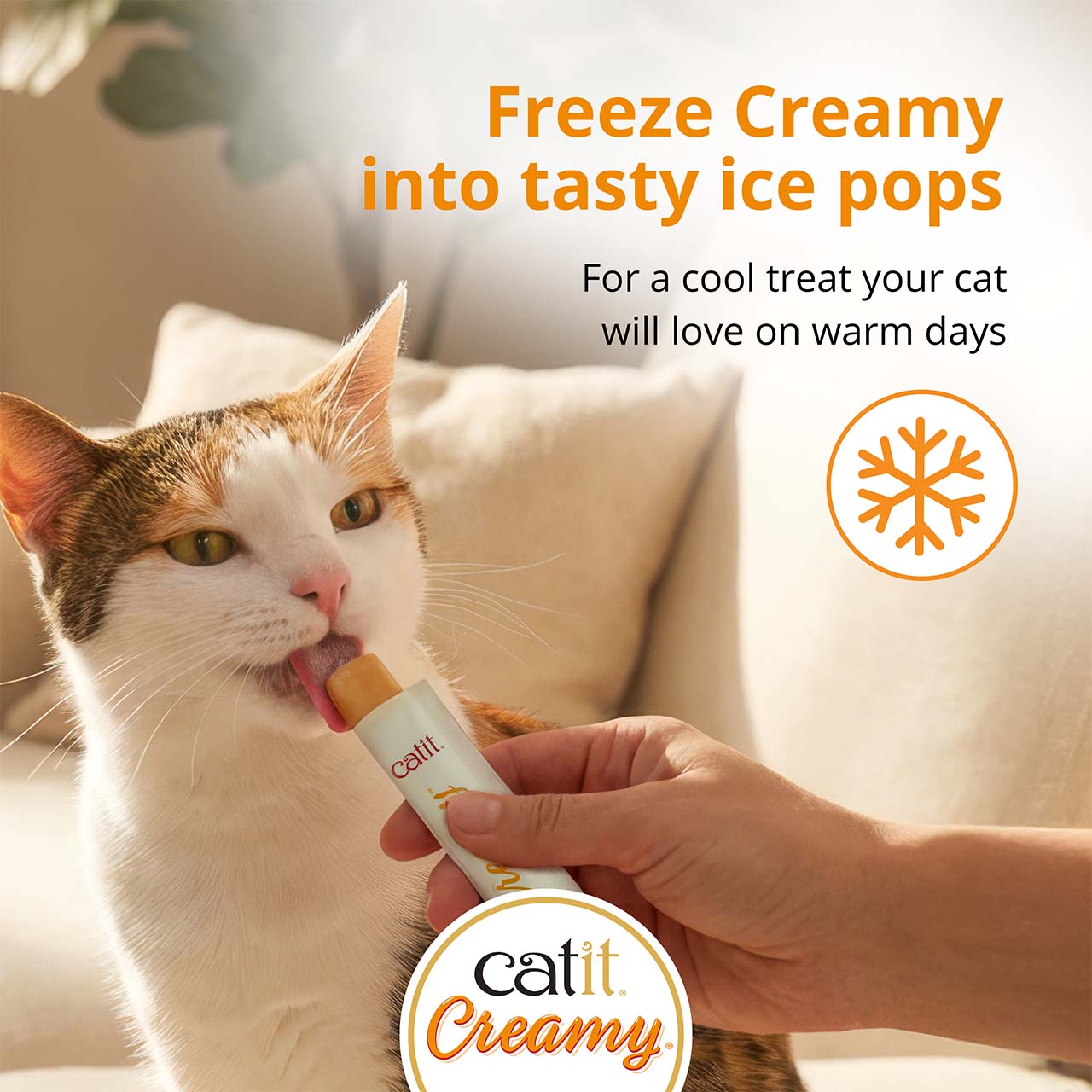 A person feeding a frozen Catit Creamy treat to a cat, suggesting it as a cool snack for warm days