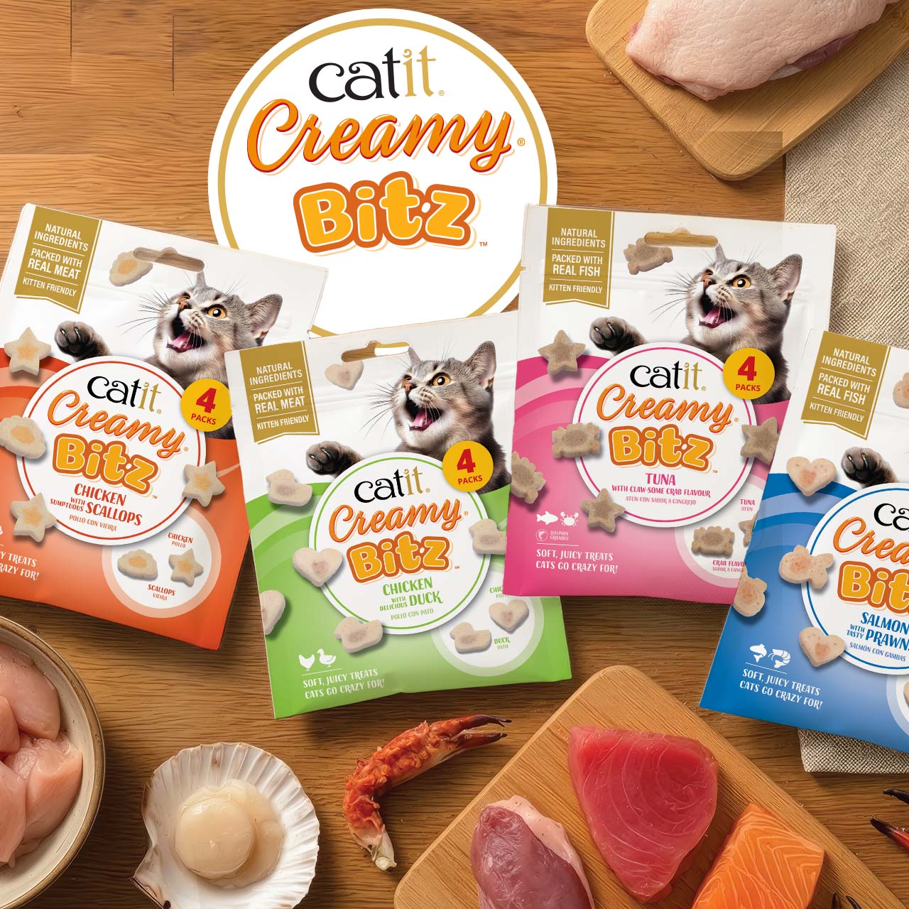 Four packages of Catit Creamy Bitz cat treats in various flavors arranged on a wooden surface with raw ingredients
