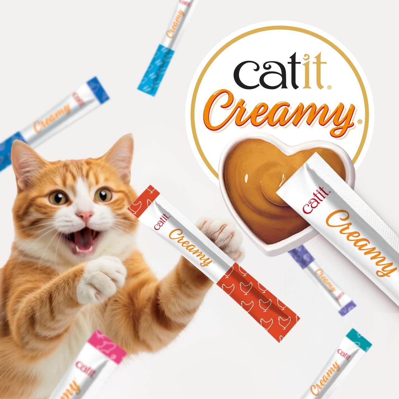 An orange tabby cat reaching for a Catit Creamy treat stick next to a heart-shaped bowl of creamy cat treat