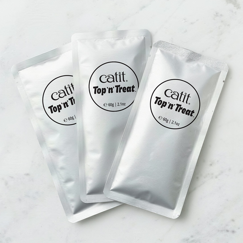 Three silver Catit Top 'n' Treat pouches on a white marble surface