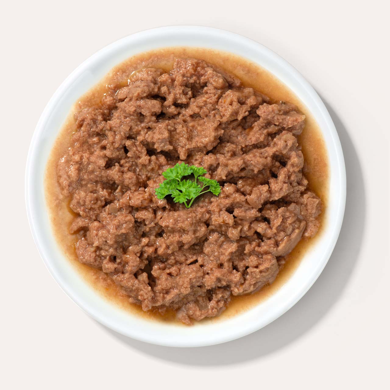 A white plate filled with wet cat food topped with a small sprig of fresh parsley