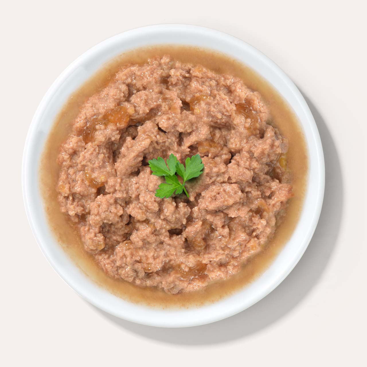 A white bowl filled with wet cat food, garnished with a small sprig of fresh parsley