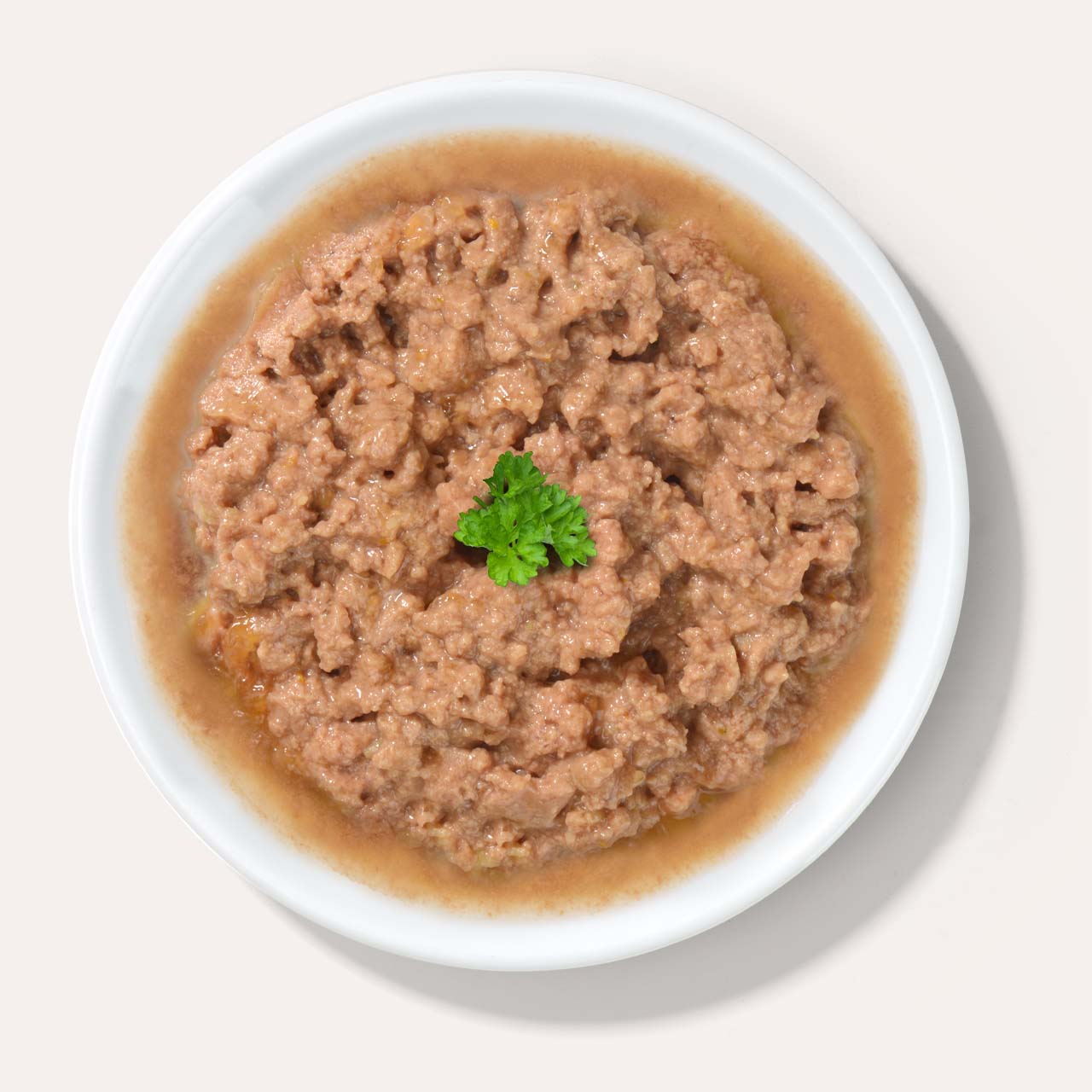 A white bowl filled with wet cat food, topped with a small sprig of fresh parsley