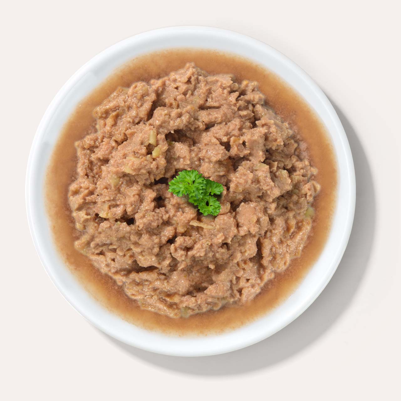 A white bowl filled with wet cat food in gravy, garnished with a small sprig of fresh parsley