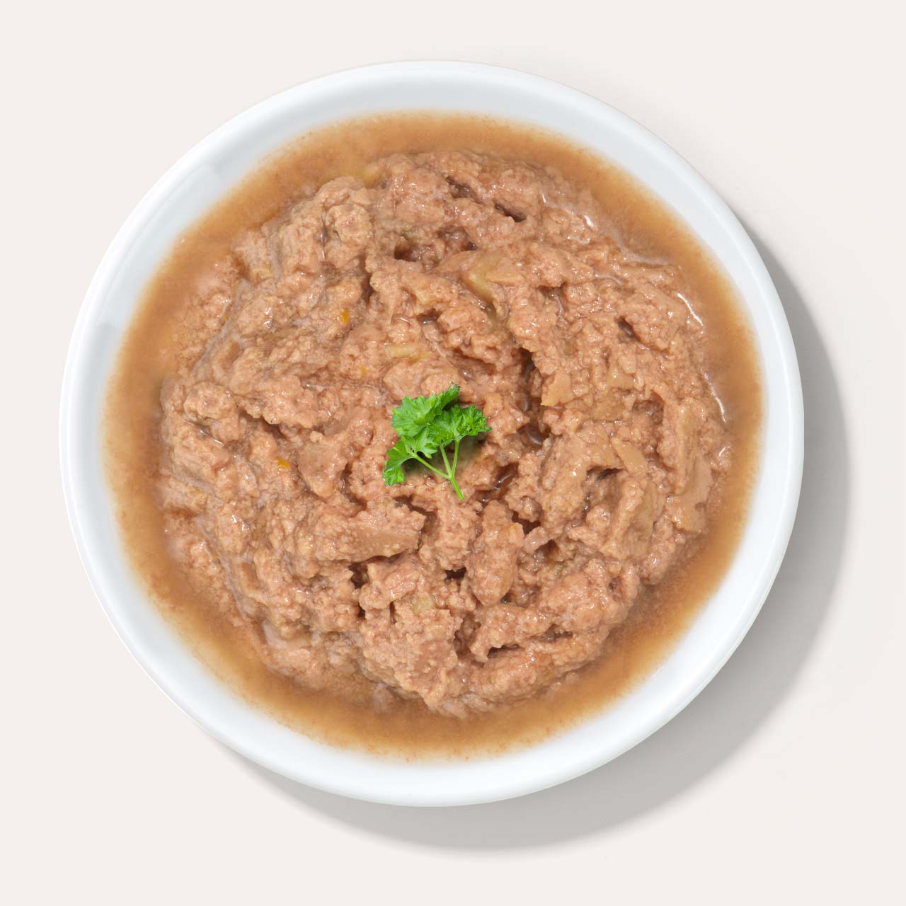 A white bowl filled with wet cat food, garnished with a small sprig of fresh parsley