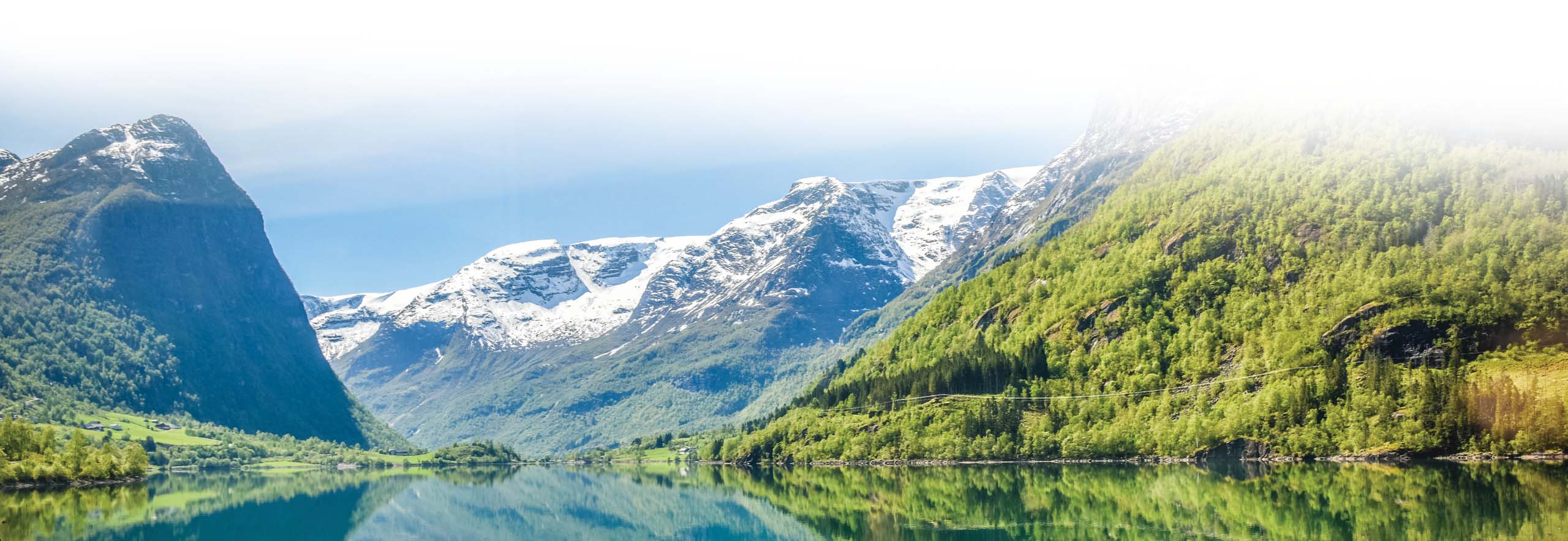 Snow-capped mountains reflected in a calm lake surrounded by lush green forests