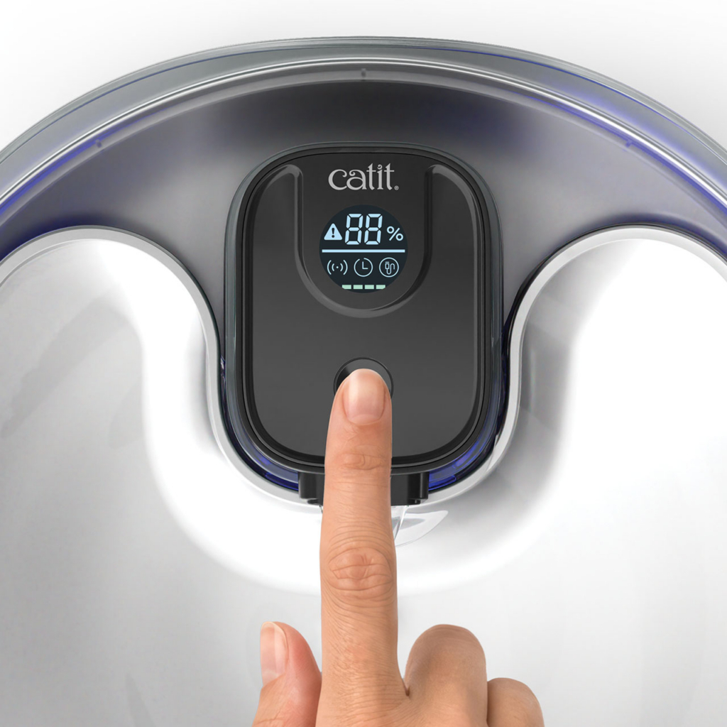 A finger pressing the button on the digital display of a Catit PIXI water fountain