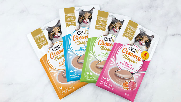 Four pouches of Catit Creamy Bisque cat treats in various flavors, featuring a cat on each package