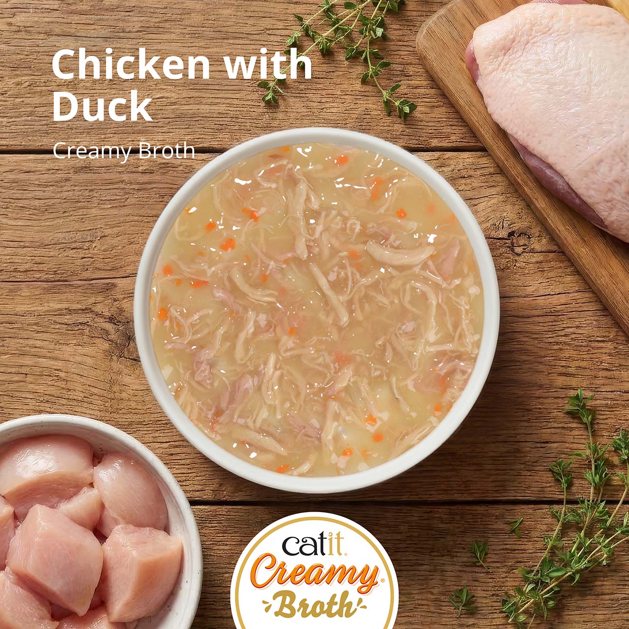 Catit Creamy Broth cat treat in chicken and duck flavor, shown in a bowl with raw meat ingredients on a wooden surface