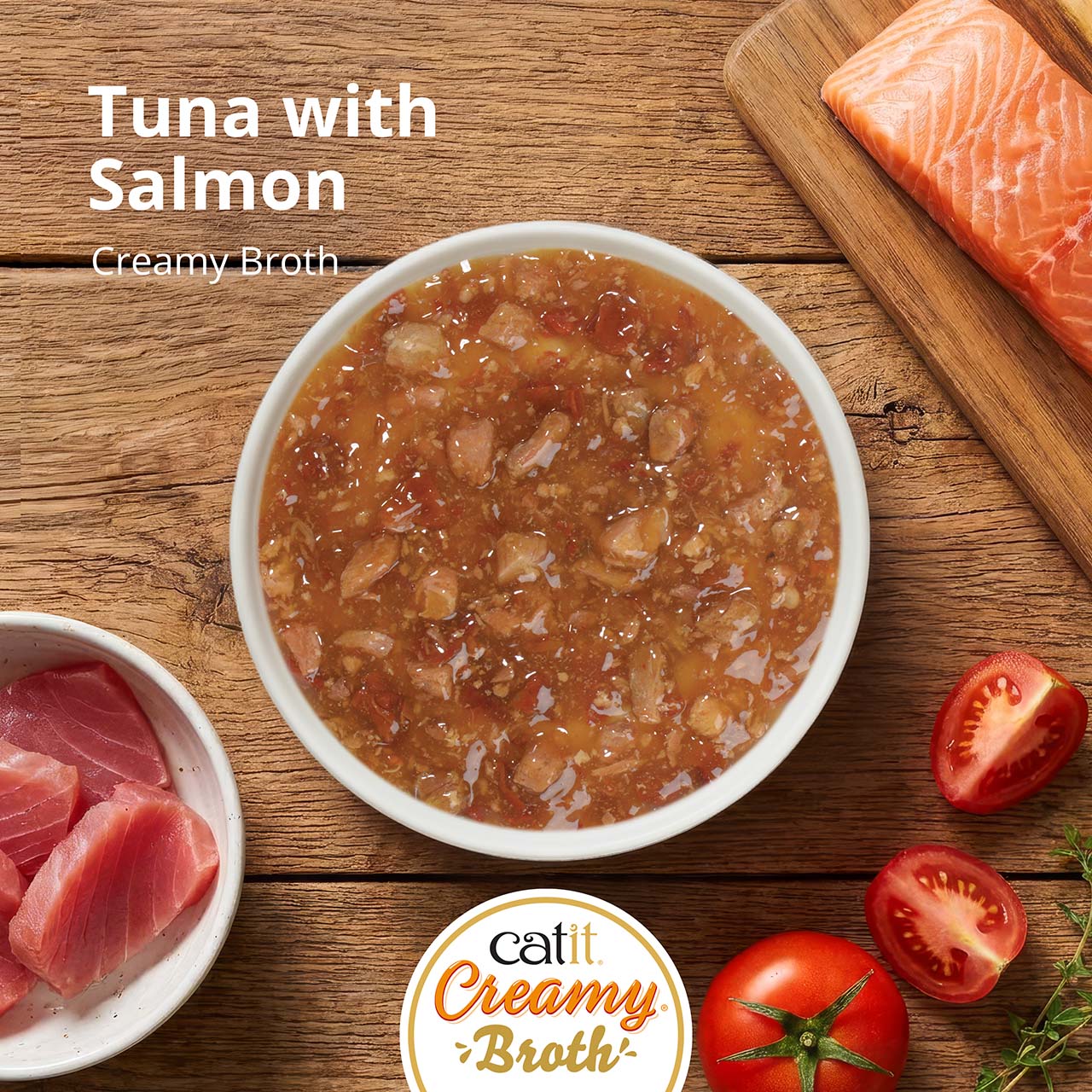 A bowl of Catit Creamy Broth cat treat featuring tuna and salmon, displayed with fresh fish and tomato ingredients
