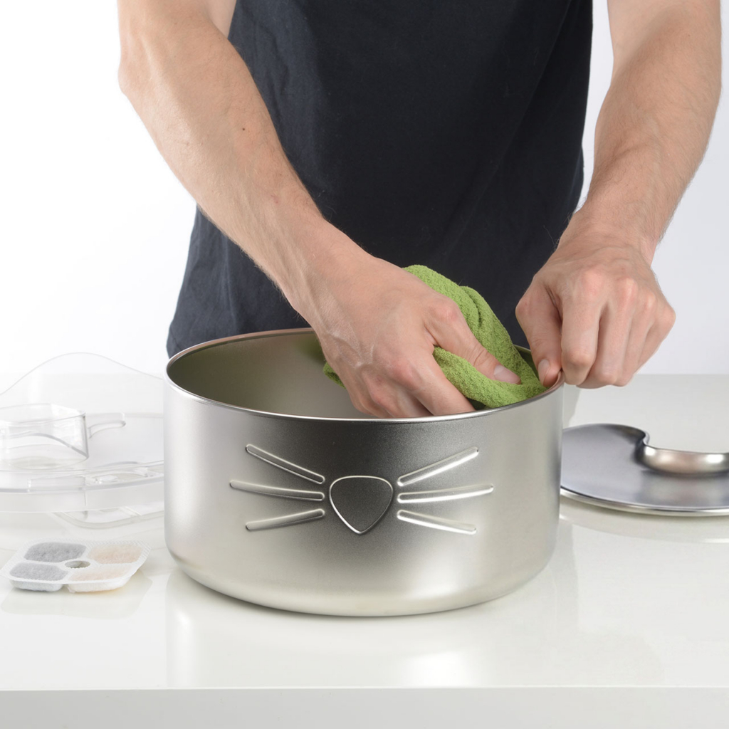 Person cleaning the stainless steel bowl of a PIXI cat water fountain with a green cloth