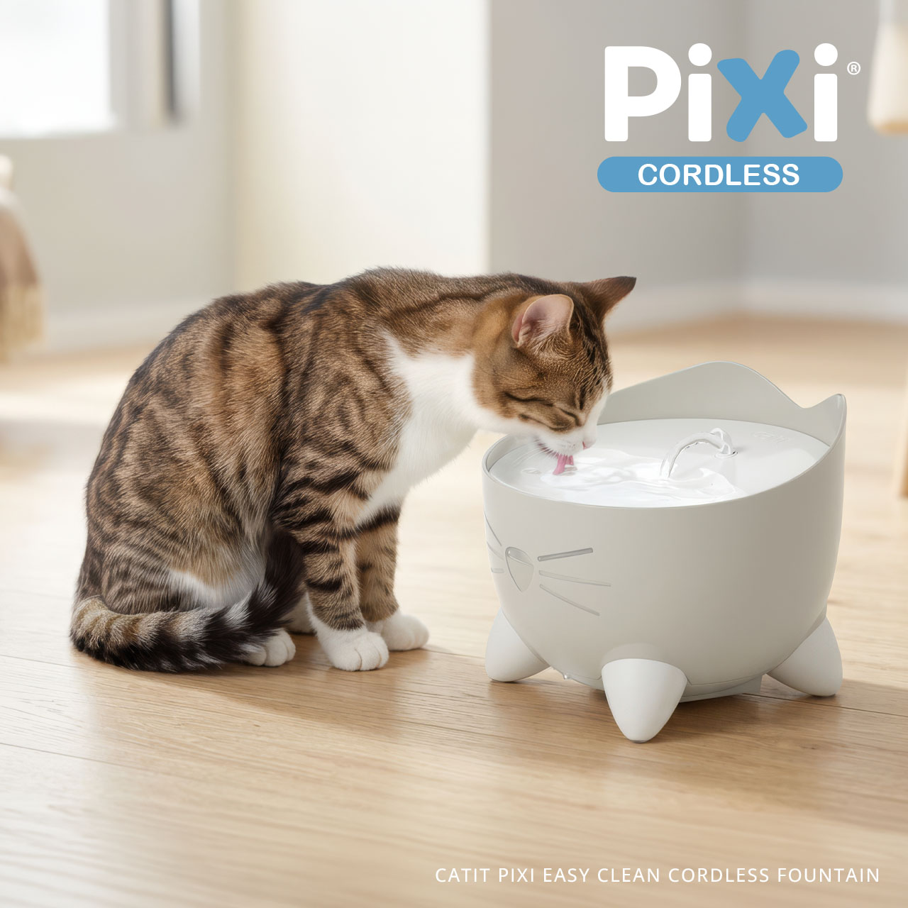 A tabby cat drinks from a light gray, cat-shaped Catit PIXI cordless water fountain on a wooden floor