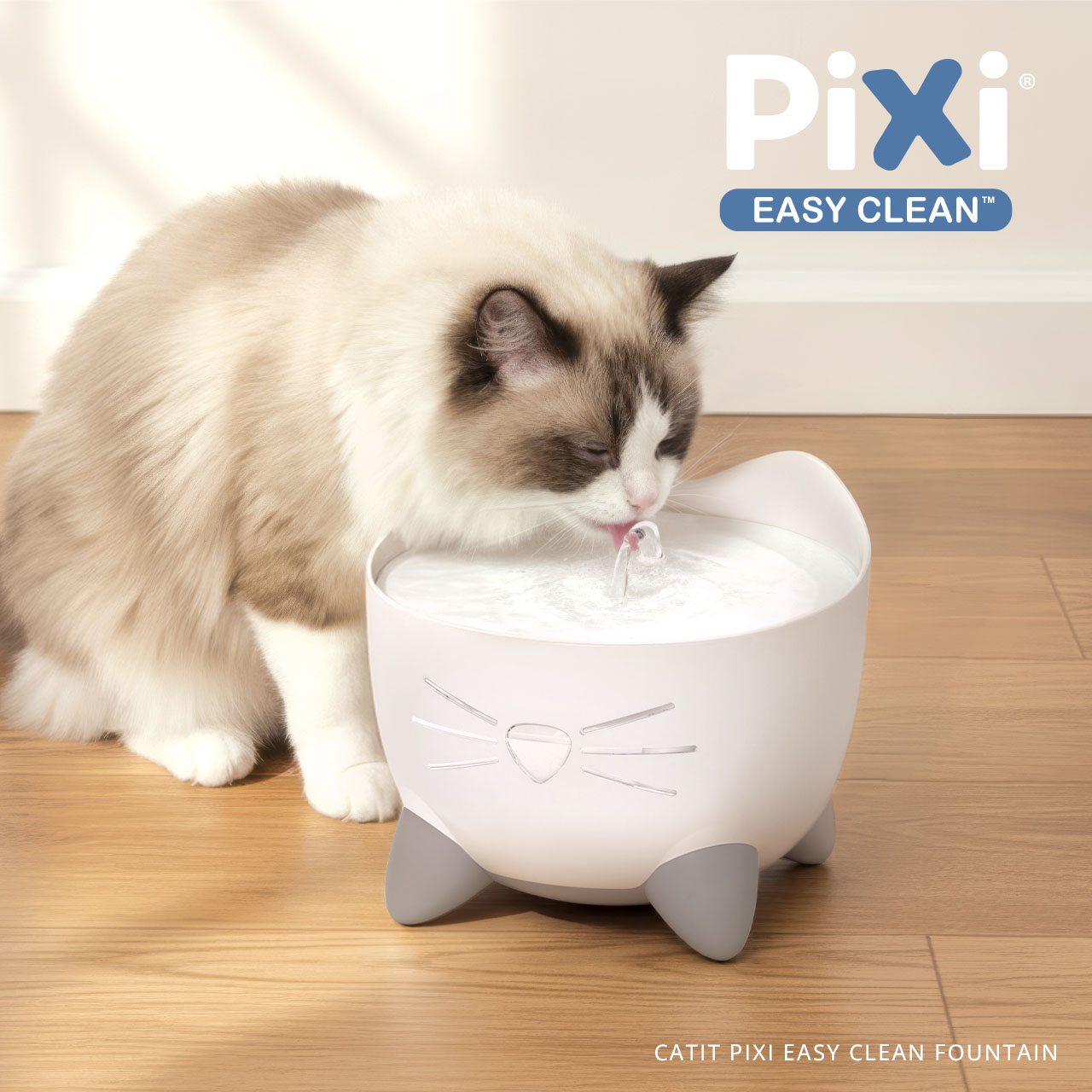 A fluffy cat drinking from a white, cat-shaped Catit PIXI Easy Clean water fountain on a wooden floor