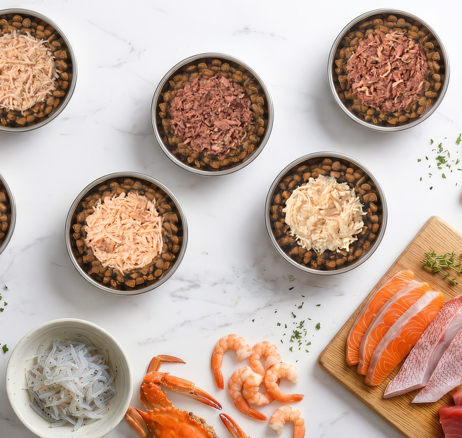Five bowls of cat food topped with various proteins, arranged on a marble surface with raw shrimp, crab, and fish fillets