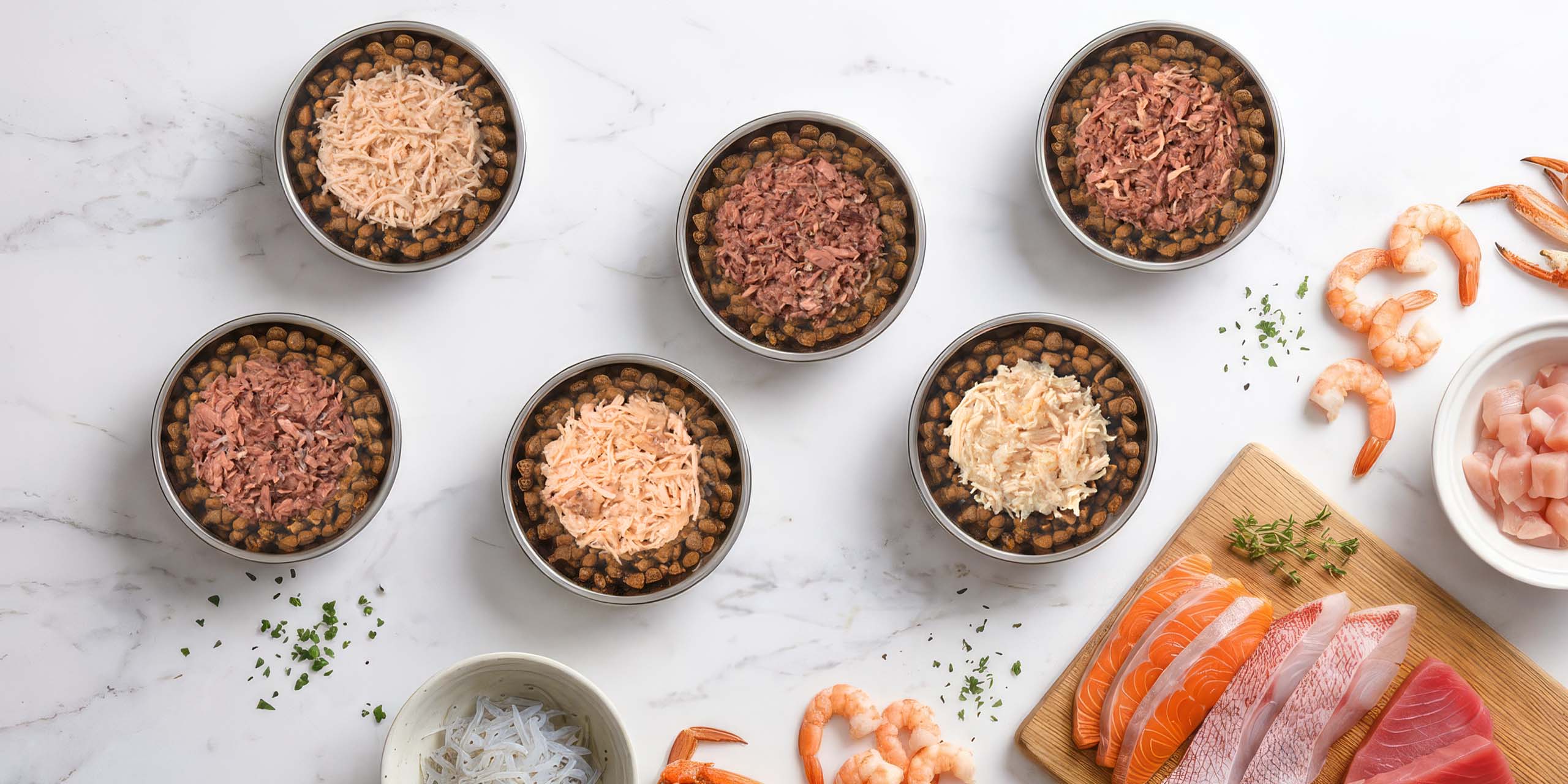 Six bowls of dry cat food topped with various fresh ingredients like shredded meat, fish, and shrimp on a marble surface