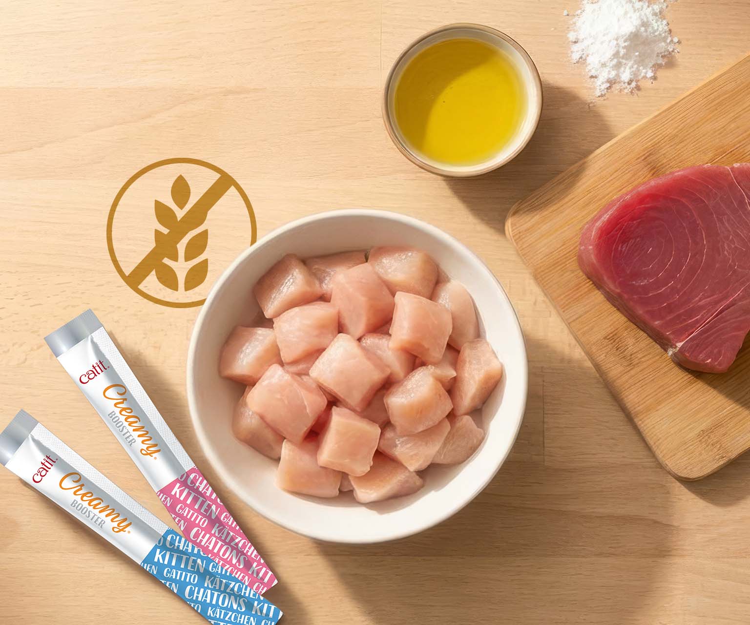 Catit Creamy Booster kitten treats displayed with raw chicken, tuna, and oil, highlighting a grain-free formula