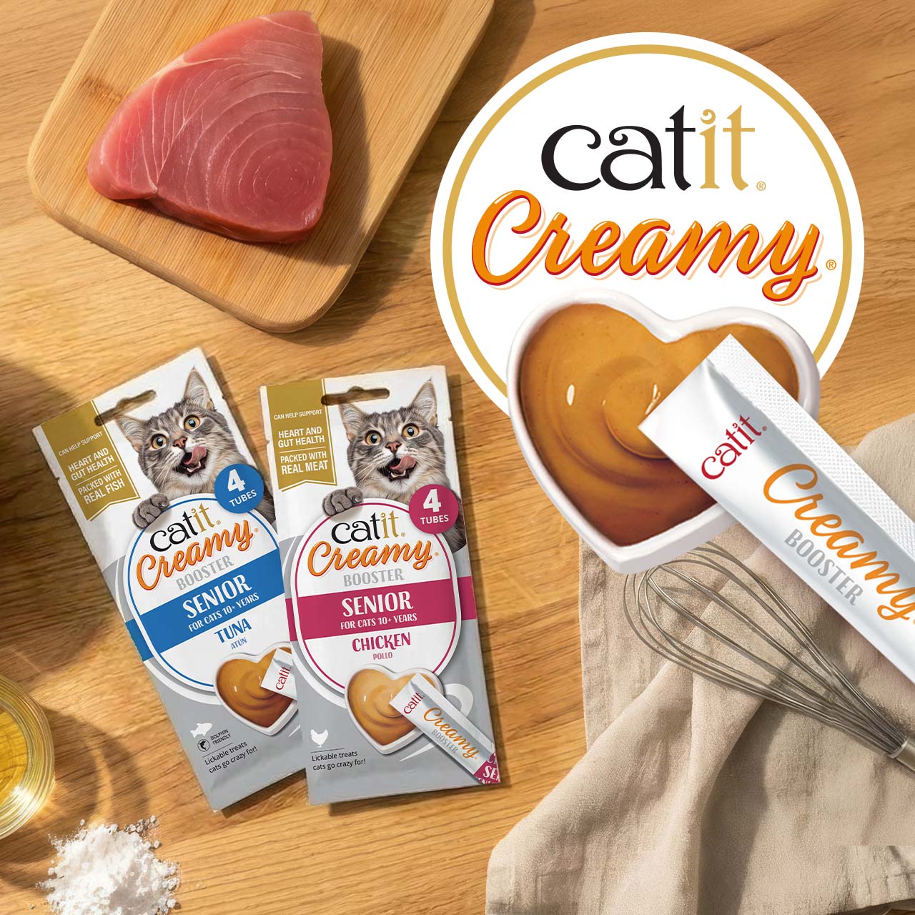 Catit Creamy Booster lickable treats for senior cats in tuna and chicken flavour laying on wooden countertop with ingredients
