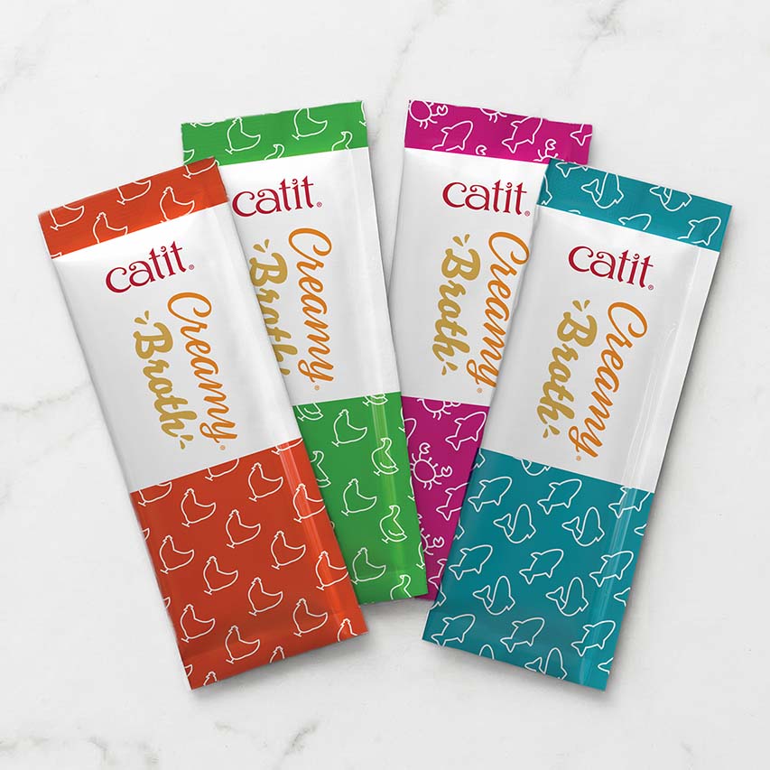 Four Catit Creamy Broth cat treat pouches in orange, green, pink, and teal packaging