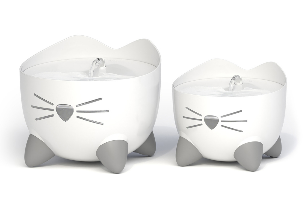 Two white PIXI cat water fountains in different sizes, each shaped like a cat head with grey feet and a nose-shaped spout