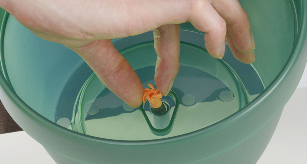 Hand placing the orange pump impeller into the base of a Catit PIXI fountain during cleaning