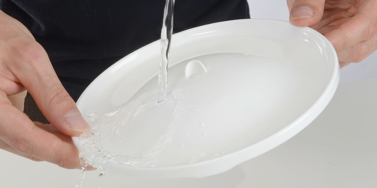 A person rinsing a white plastic component of a Catit PIXI fountain under running water