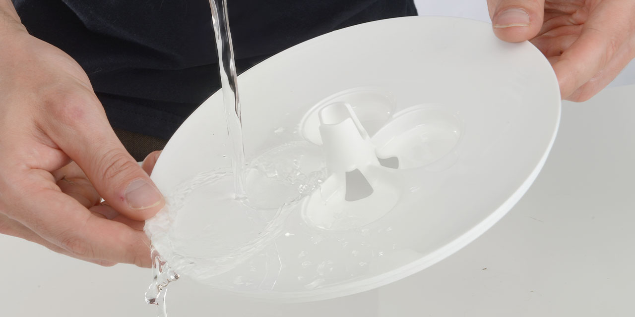 Hands rinsing a white plastic flower fountain component under running water