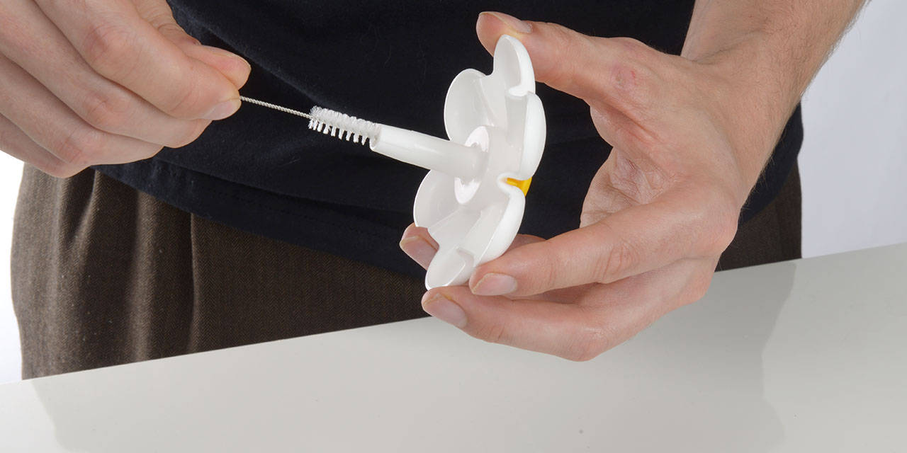 Hands cleaning the flower attachment of a Catit PIXI fountain with a small brush