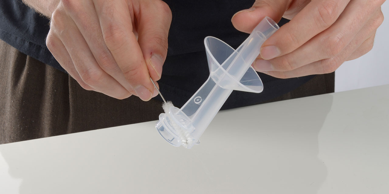 Hands cleaning the plastic pump housing of a Catit PIXI fountain with a small brush